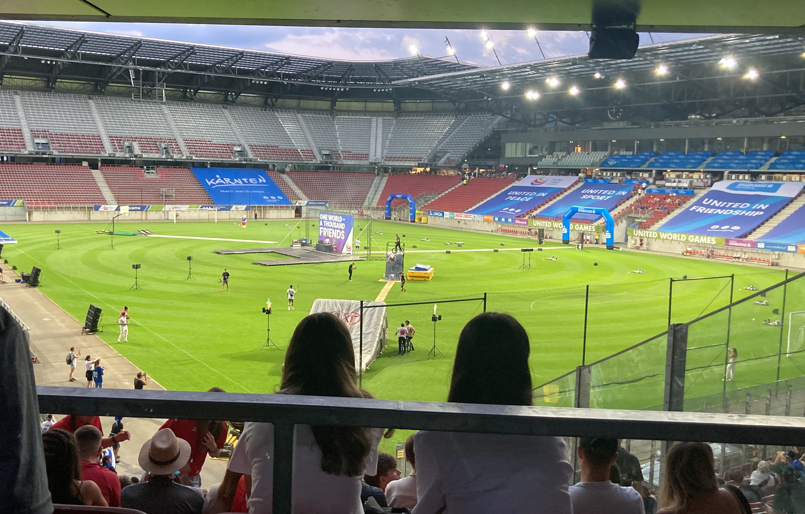 Blick von der Tribüne des Wörthersee Stadions in Klagenfurt während der United World Games, mit einem großen Fußballfeld und Veranstaltungsbannern.