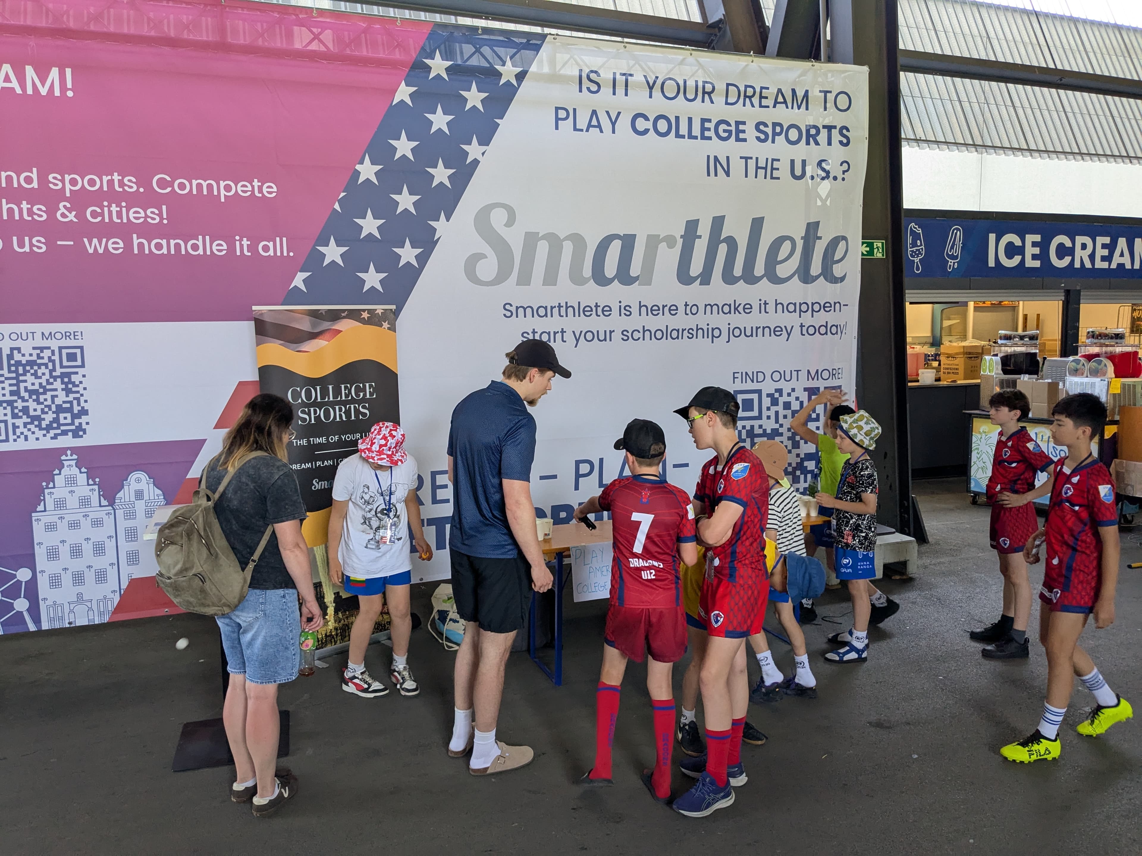 Ein großes Smarthlete-Werbebanner an einem Informationsstand mit der Aufschrift 'Is it your dream to play college sports in the U.S.?' mit jungen Athleten davor.