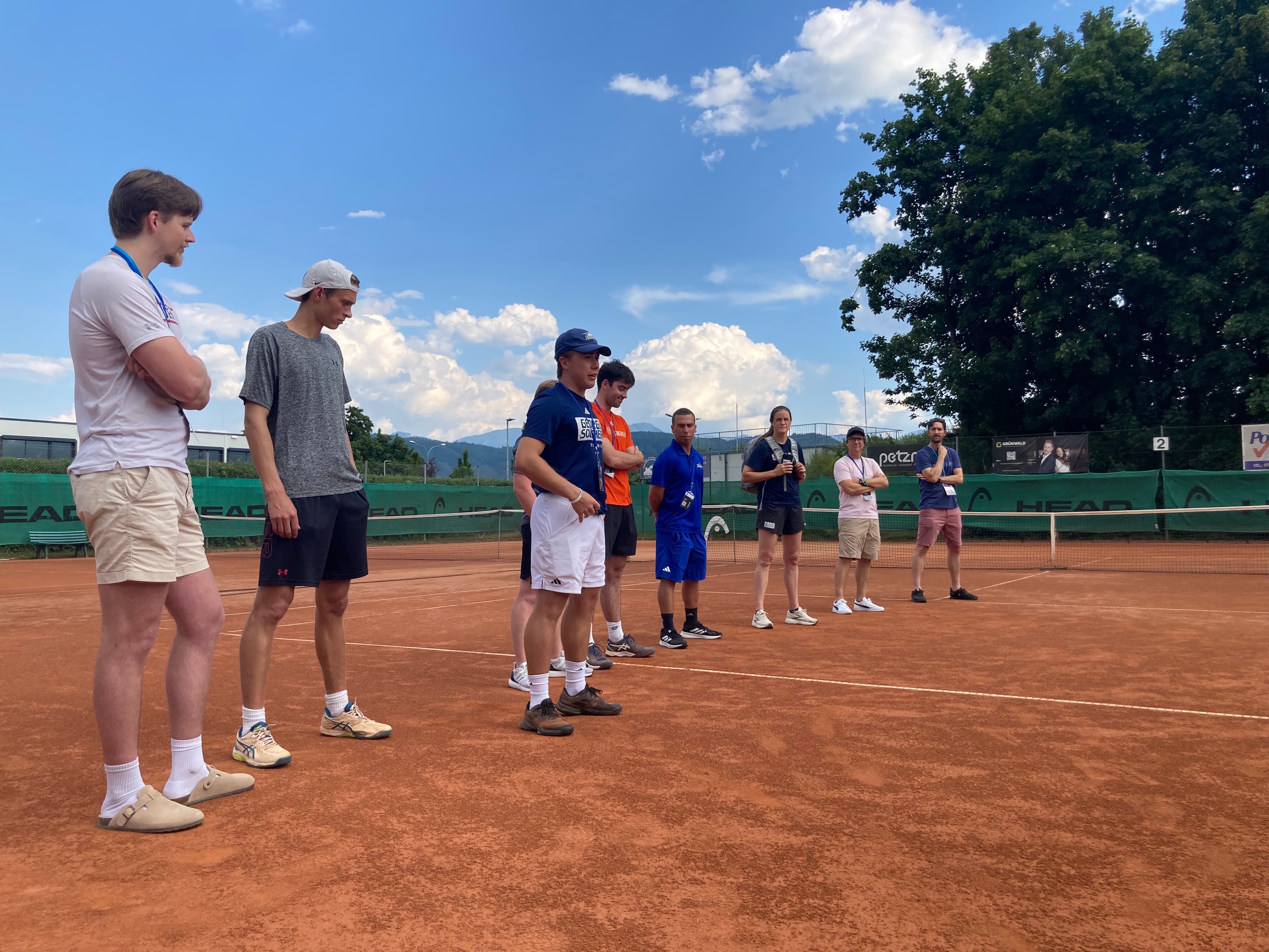 Eine Gruppe von College-Tennistrainern und Recruiting-Experten auf einem Sandplatz.