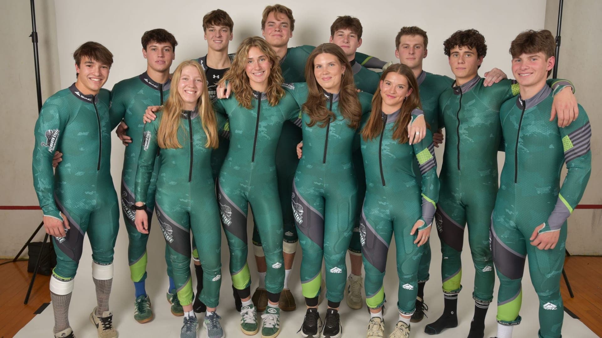 Ski-Team der Plymouth State University | Julia Müller Das Ski-Team der Plymouth State University vor einer weißen Wand in grünen Skirennsuits.