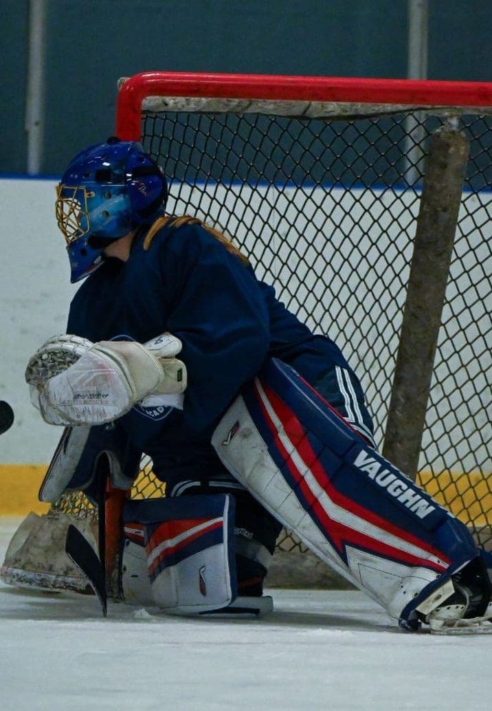 College-Eishockey-Torhüter bewacht das Tor | Smarthlete Ein Eishockey-Torhüter in Blau und Rot bewacht das Tor.
